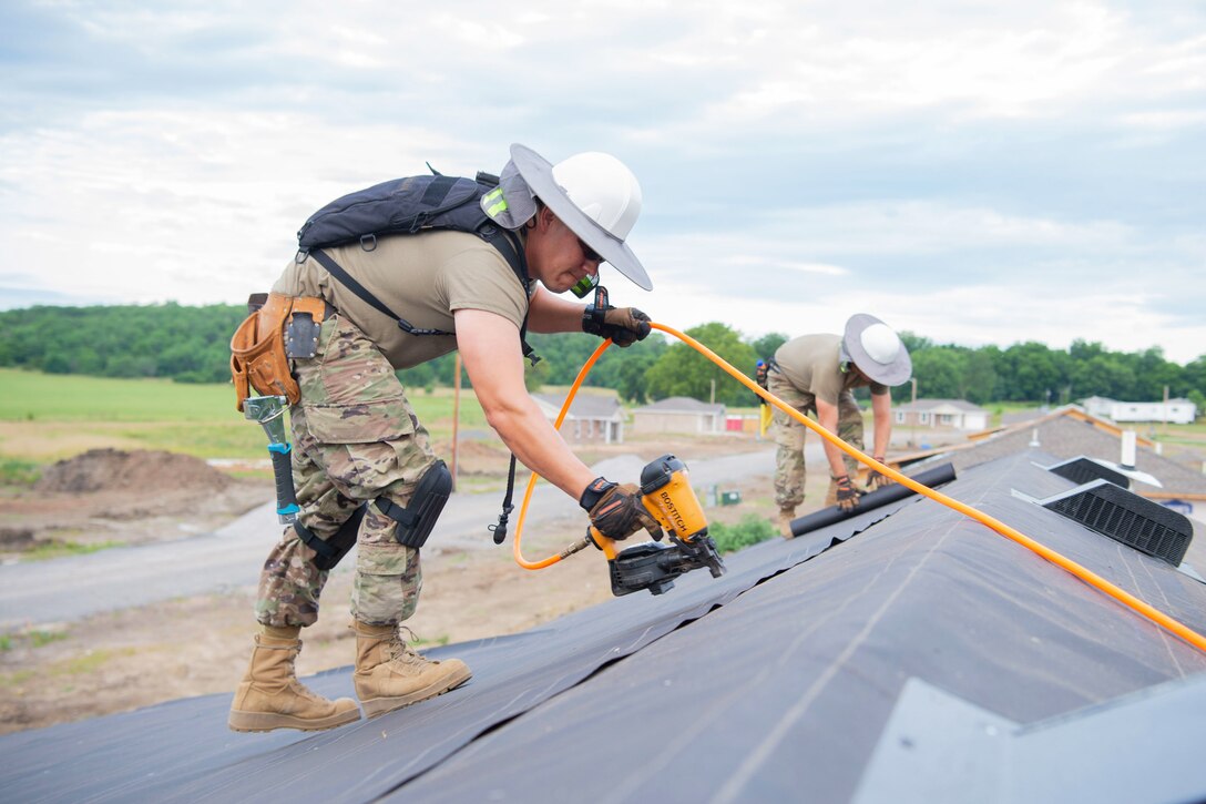 Two airmen used tools to work on top of a roof.