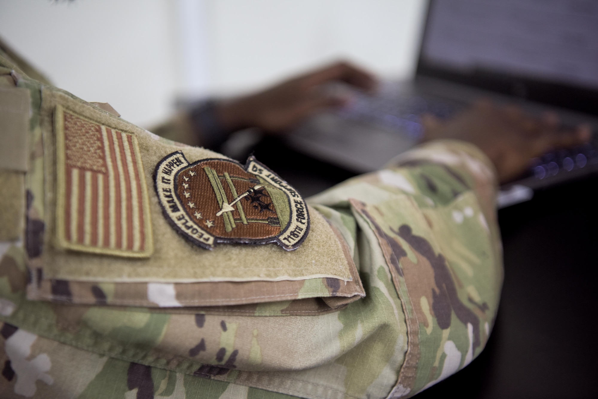 A 718th Force Support Squadron rests on the uniform sleeve of an Airman as he types on a laptop.