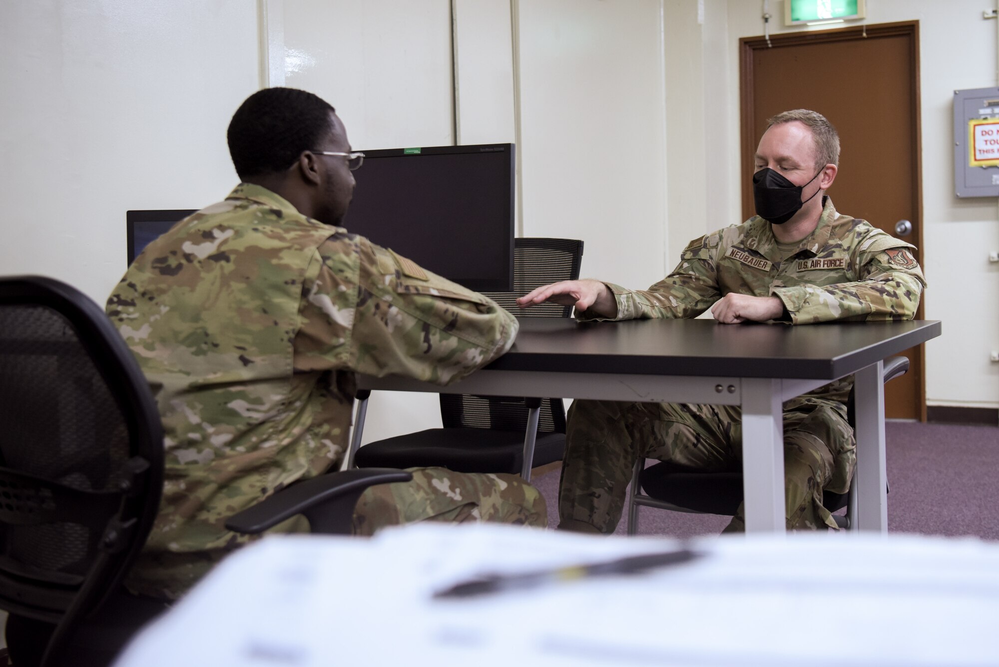 Two Airmen sit at a table talking to each other.