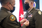 An Army officer in a brown uniform pins a Purple Heart medal on another officer in a brown uniform.