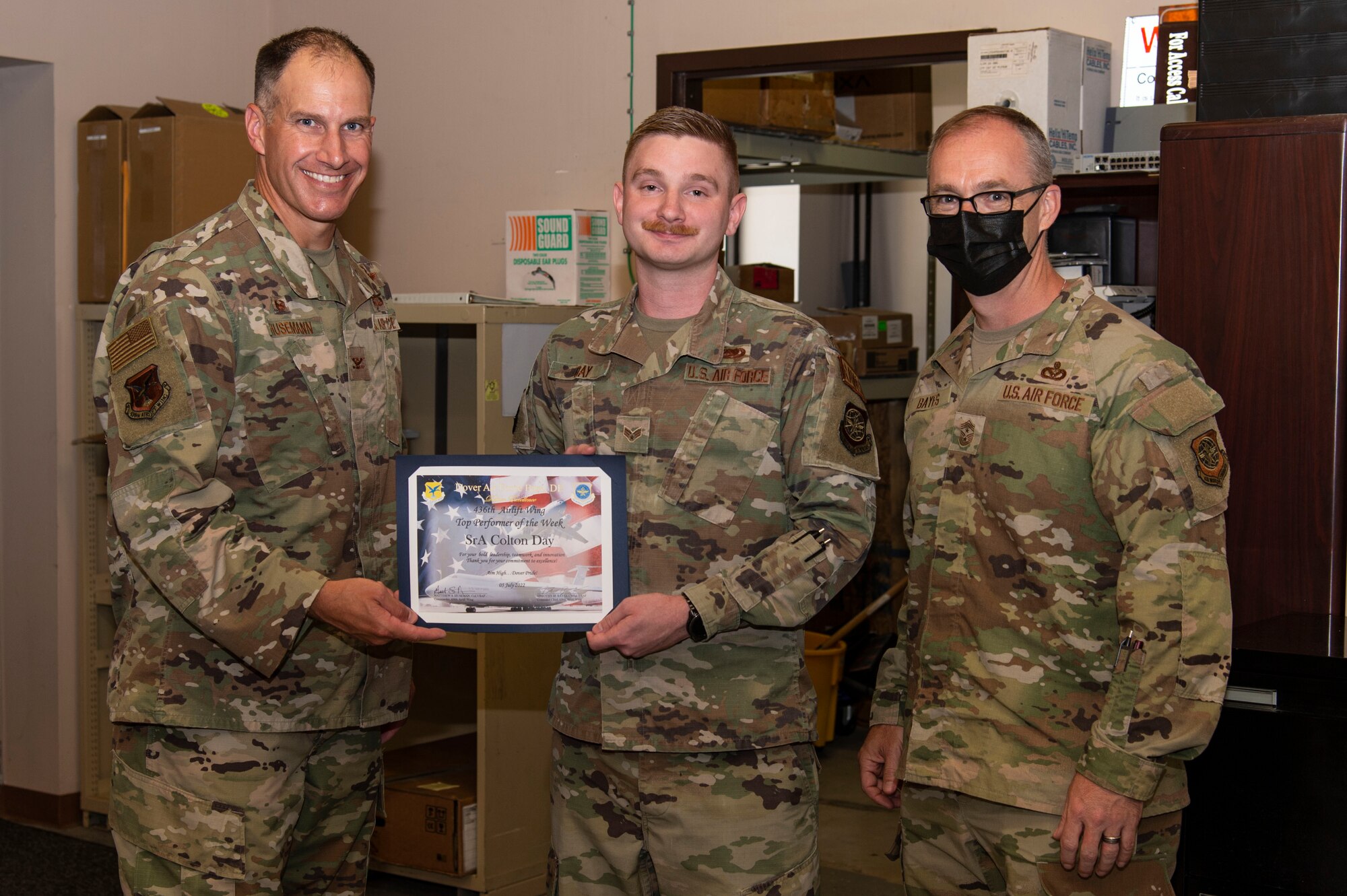 Col. Matt Husemann, left, 436th Airlift Wing commander, presents Senior Airman Colton Day, center, 436th Operations Support Squadron radar airfield weather systems technician, with a certificate as the week’s Top Performer on Dover Air Force Base, Delaware, July 5, 2022. Day was coined by Husemann and Chief Master Sgt. Timothy Bayes, right, 436th AW command chief, for outstanding performance. (U.S. Air Force photo by Roland Balik)