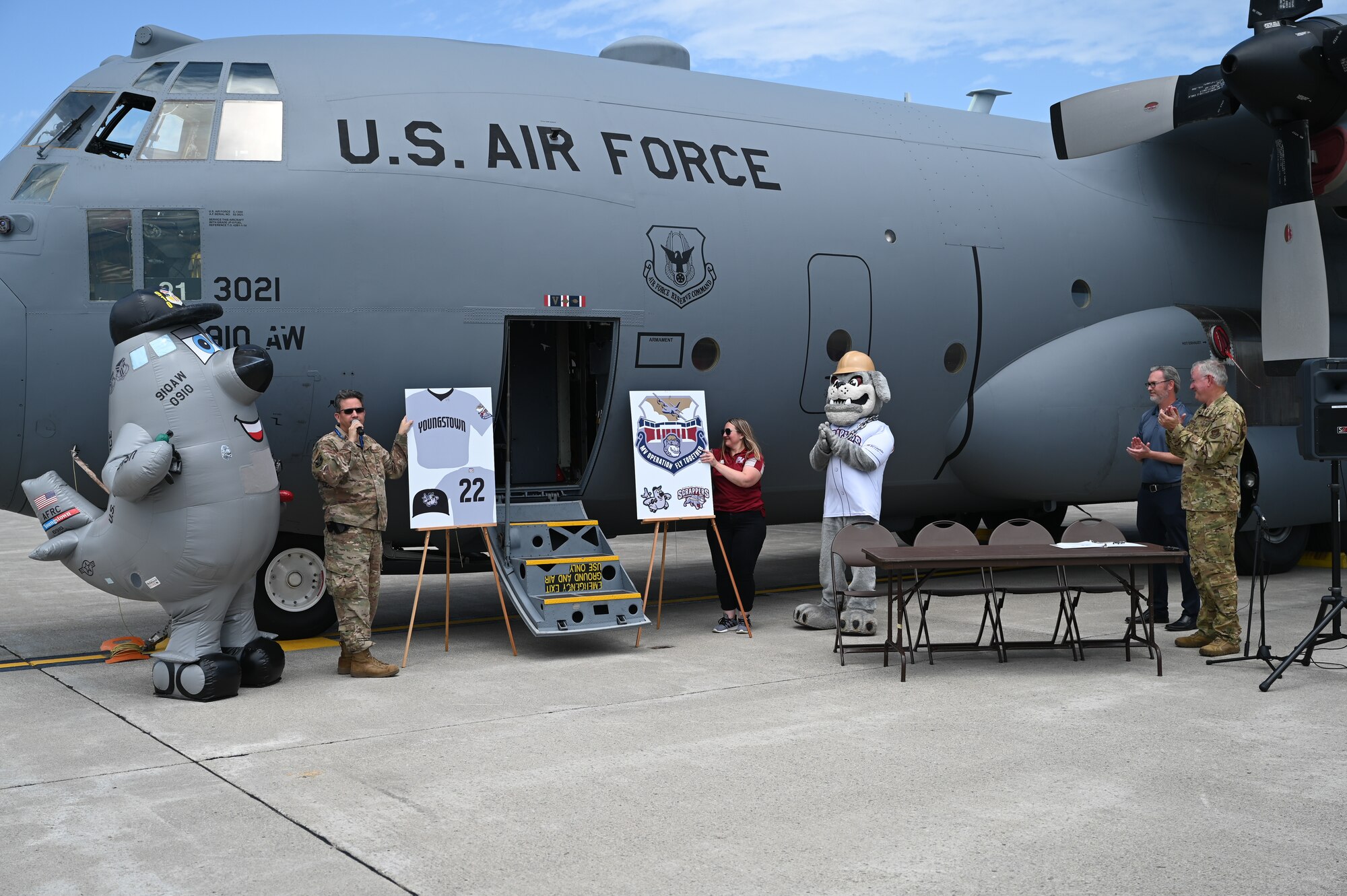 Senior Master Sgt. Bob Barko Jr., 910th Airlift Wing public affairs superintendent, and Heather Sahli, assistant general manager of marketing for the Mahoning Valley Scrappers baseball team, unveil posters displaying artwork to be featured on items worn by team players at an upcoming game, June 29, 2022, at Youngstown Air Reserve Station, Ohio.