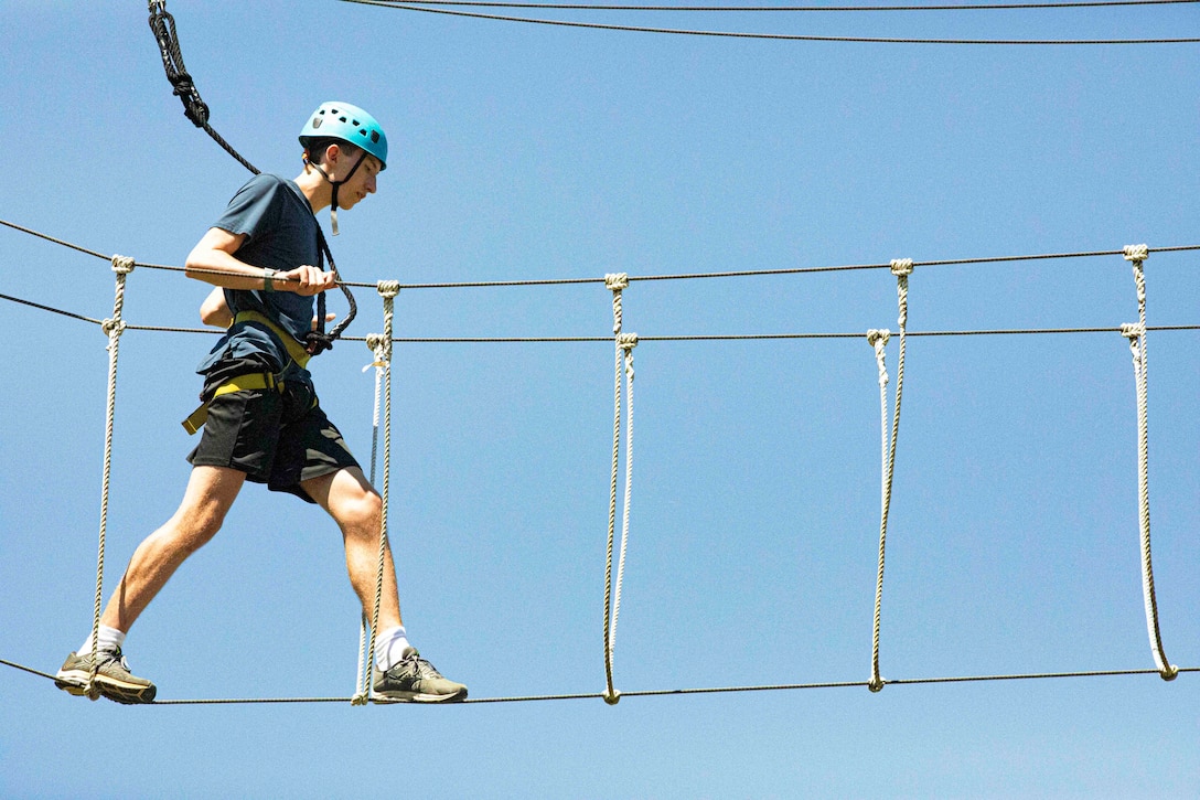 A teen wearing protective gear walks across a rope.