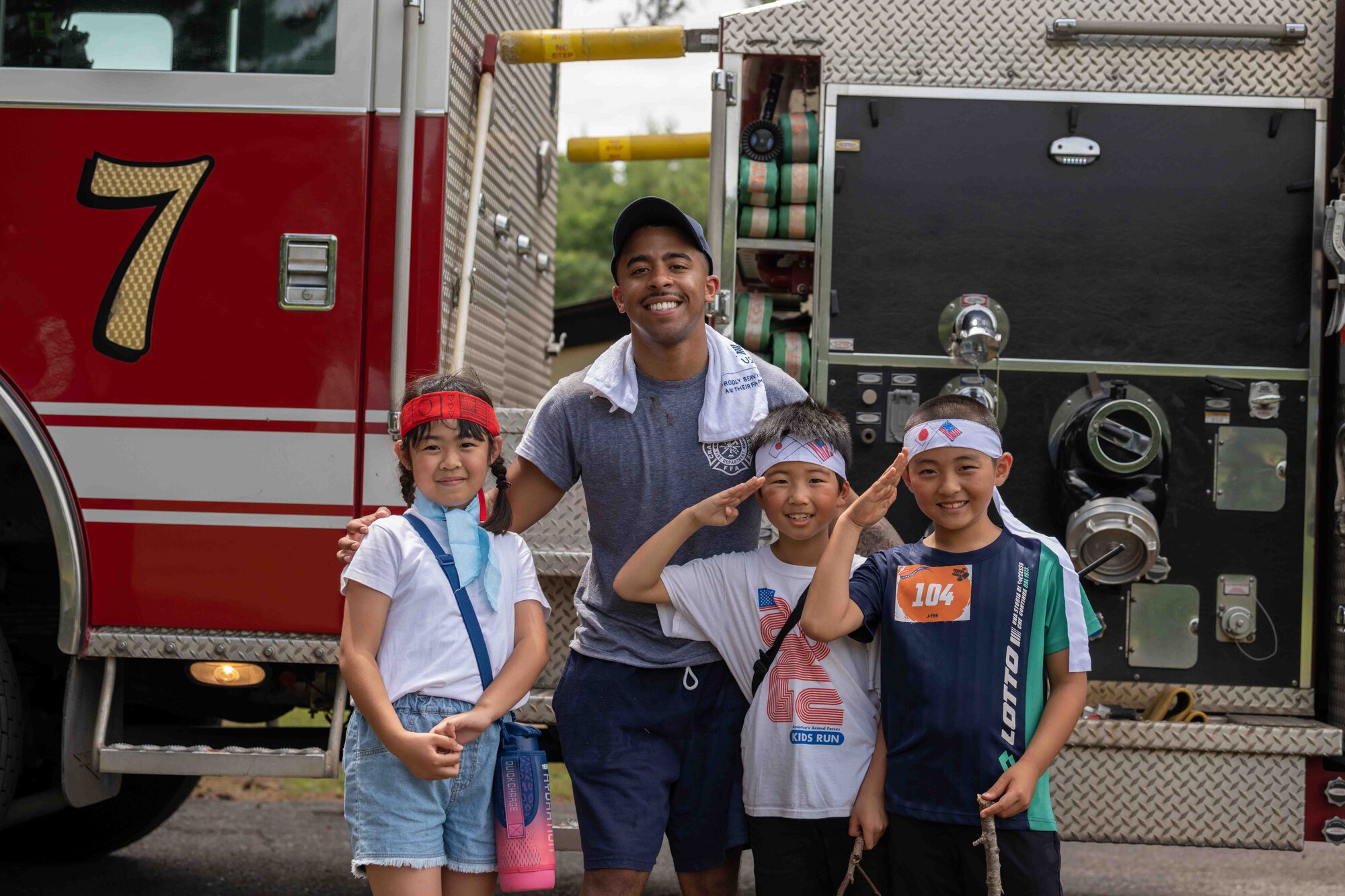 U.S. Air Force Airman 1st Class Daniel Elliot, 35th Civil Engineer Squadron firefighter, and young participants pose in front of a fire truck during the annual Misawa Mudder at Misawa Air Base, Japan, July 2, 2022.