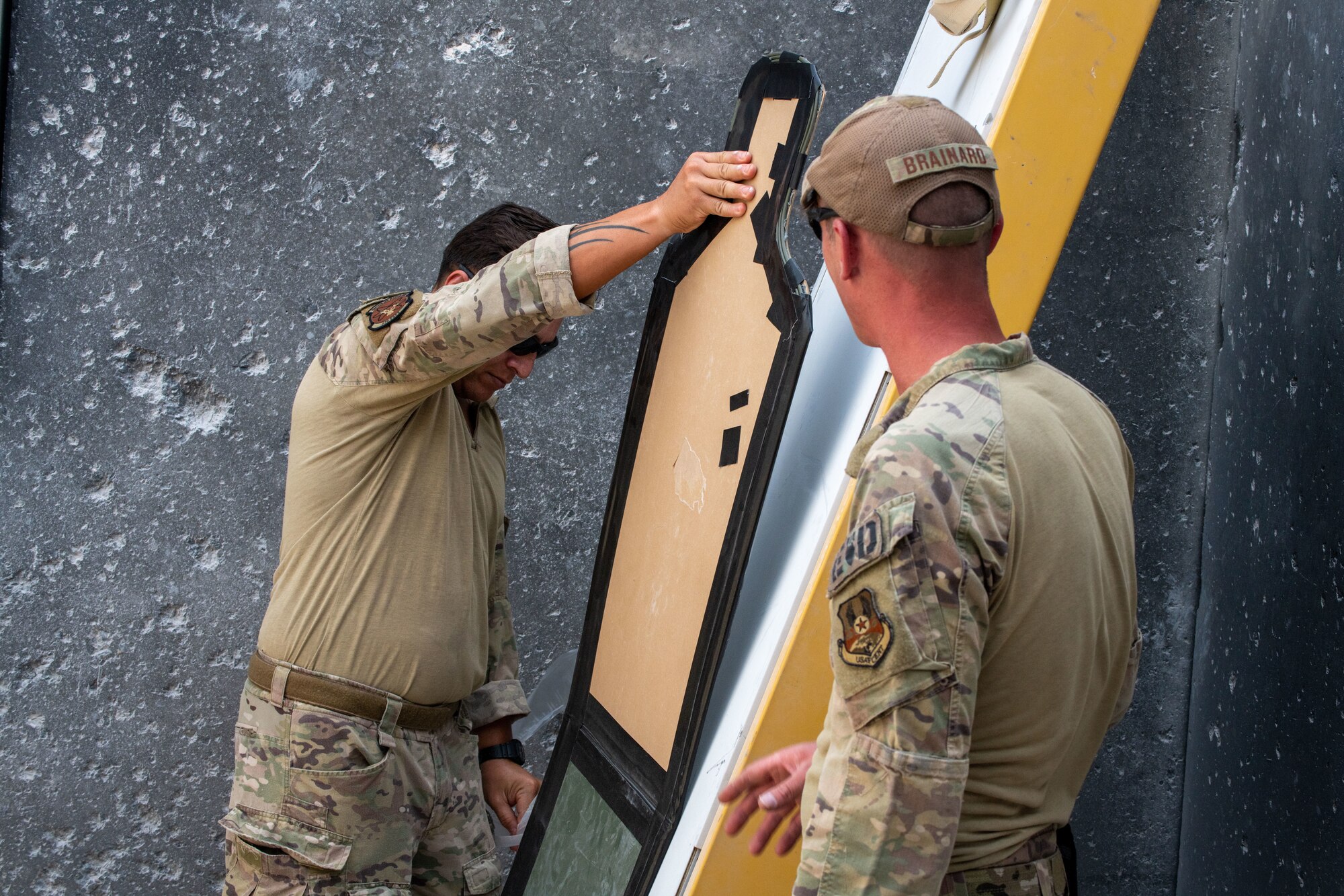 U.S. Air Force Staff Sgt. Josiah Brainard and Staff Sgt. George Cochran, explosive ordinance disposal technicians with the 379th Expeditionary Civil Engineer Squadron, place a cardboard silhouette, on a door frame on Al Udeid Air Base, Qatar, July 1, 2022. The cardboard is outlined with detonating cord, which is designed to create a large hole in the door. (U.S. Air National Guard photo by Airman 1st Class Constantine Bambakidis)