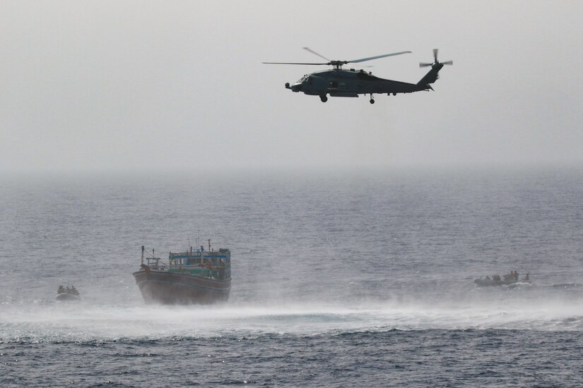 A helicopter flies above a military ship.