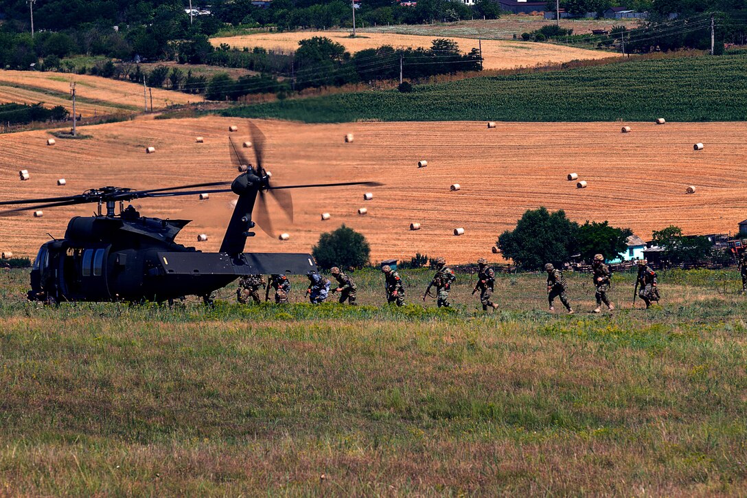Soldiers walk across a field where a helicopter is waiting.
