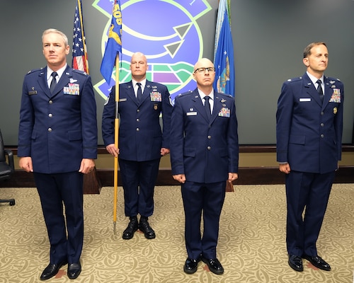 Photo of three USAF Airmen standing at attention and one Airmen standing behind them holding the unit flag