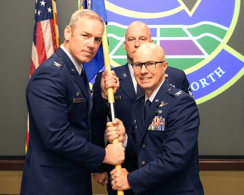 Photo of U.S. Airmen holding unit guidon flag with Airman standing in the background