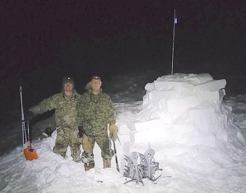 Photo of Lt. Col. (Dr.) Jesse Wells and an Army specialist posing outside of their igloo on survival night during the Winter Medicine Course.