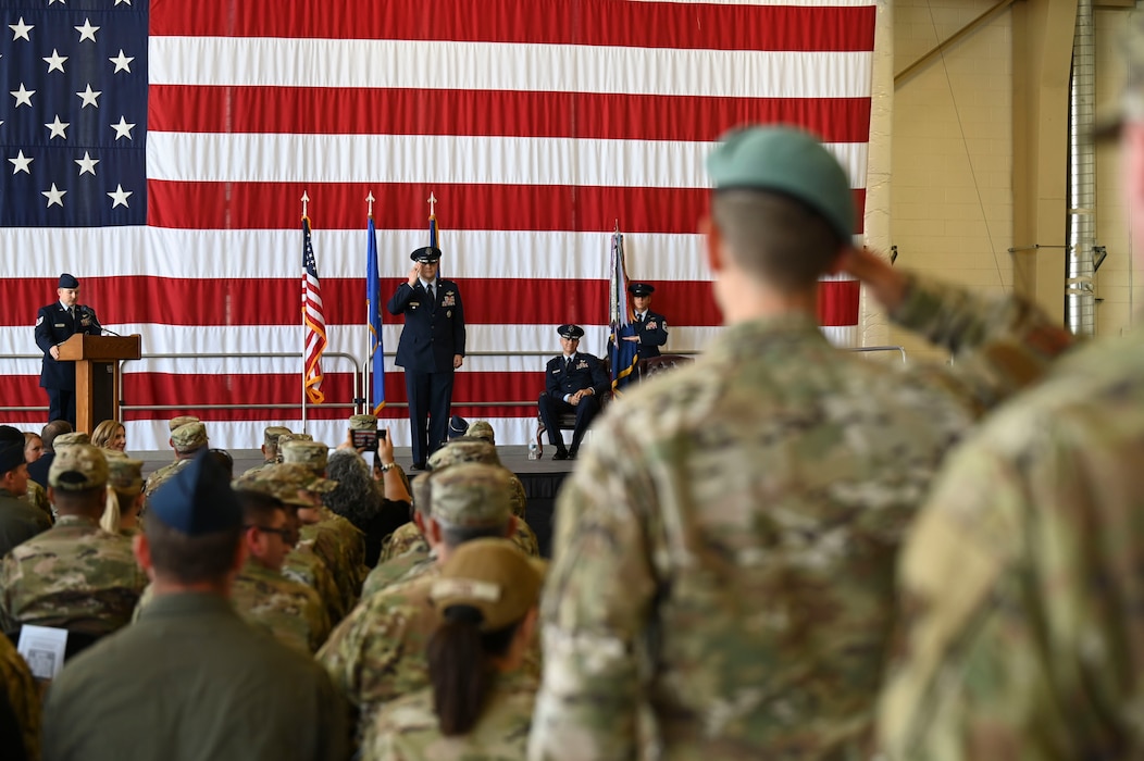 Two airmen pass the flag, one airmen looks on.