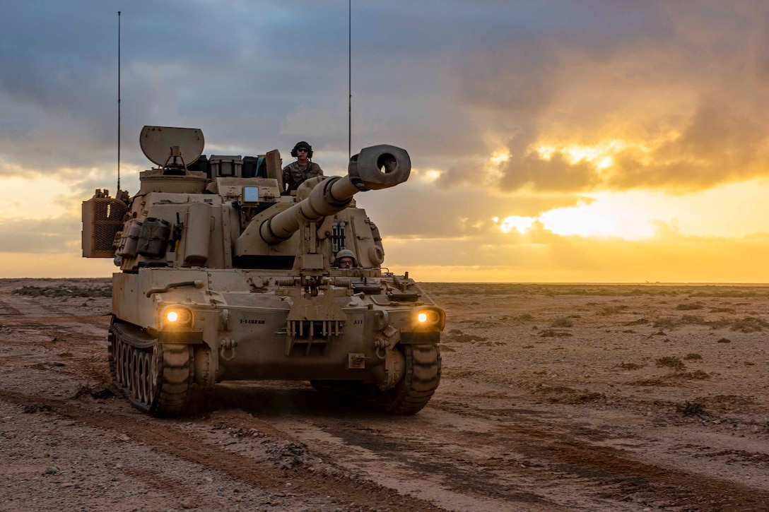 A guardsman rides in a tank through desert terrain.