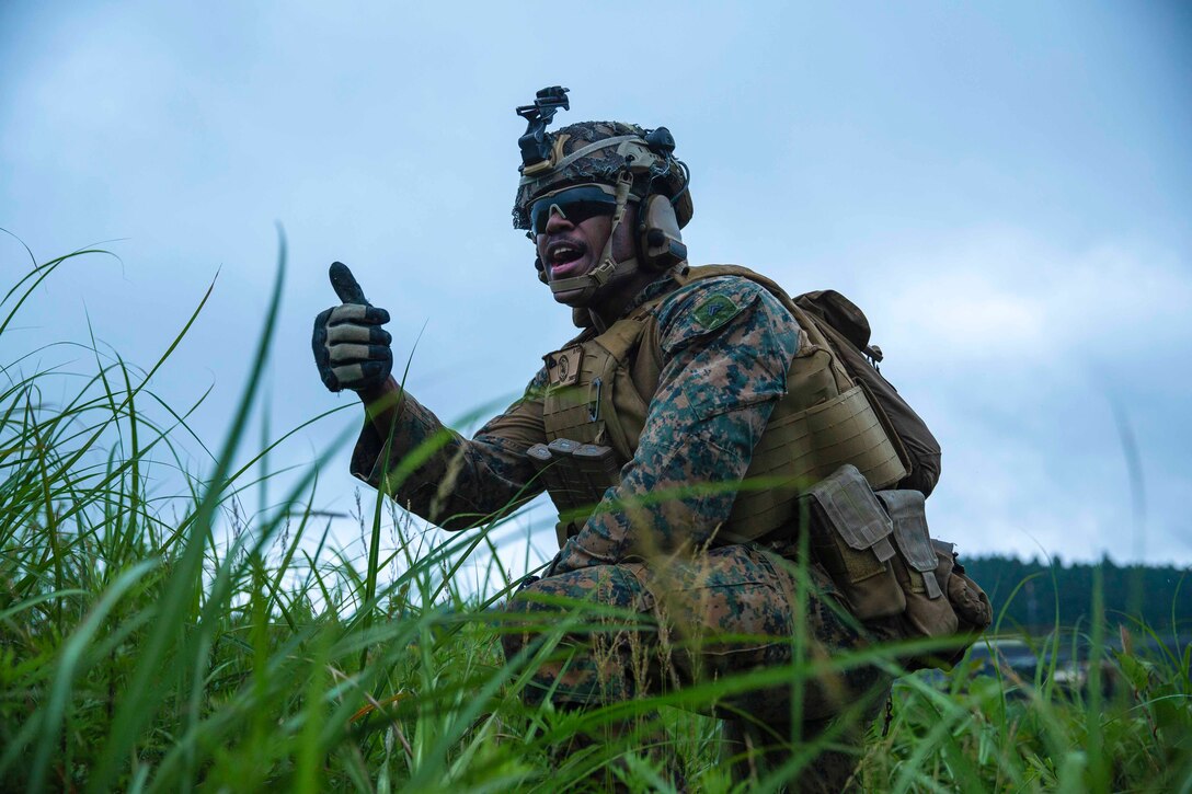 A Marine kneels in grass giving the thumbs up.