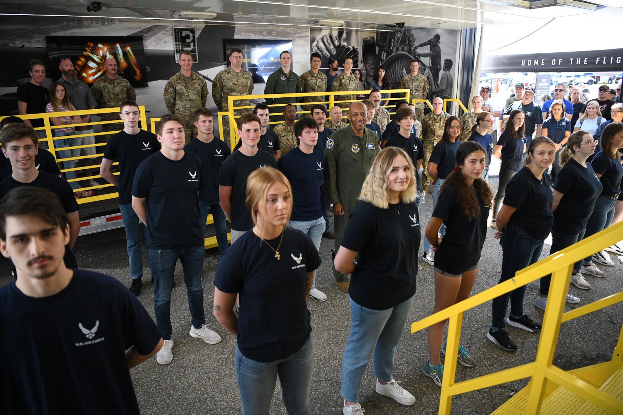 Air Force Chief of Staff Gen. CQ Brown, Jr., (in flight suit, center of frame) posed for a group photo with 23 future Airmen, Air Force recruiters and Air Force family members inside a national recruiting asset called "The Hangar," at the Road America race course near Elkhart Lake, Wisconsin, July 3, 2022.