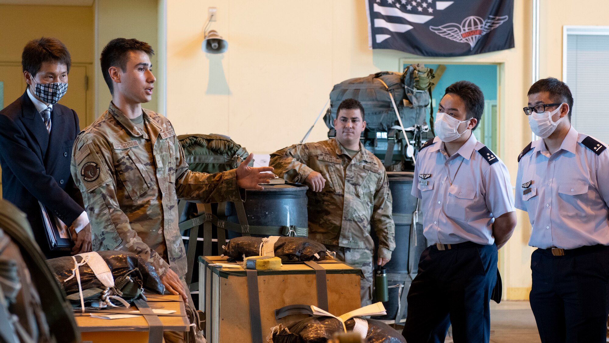 An Airman shows a formally dressed group of Japanese cadets cargo pallets attached to parachutes.