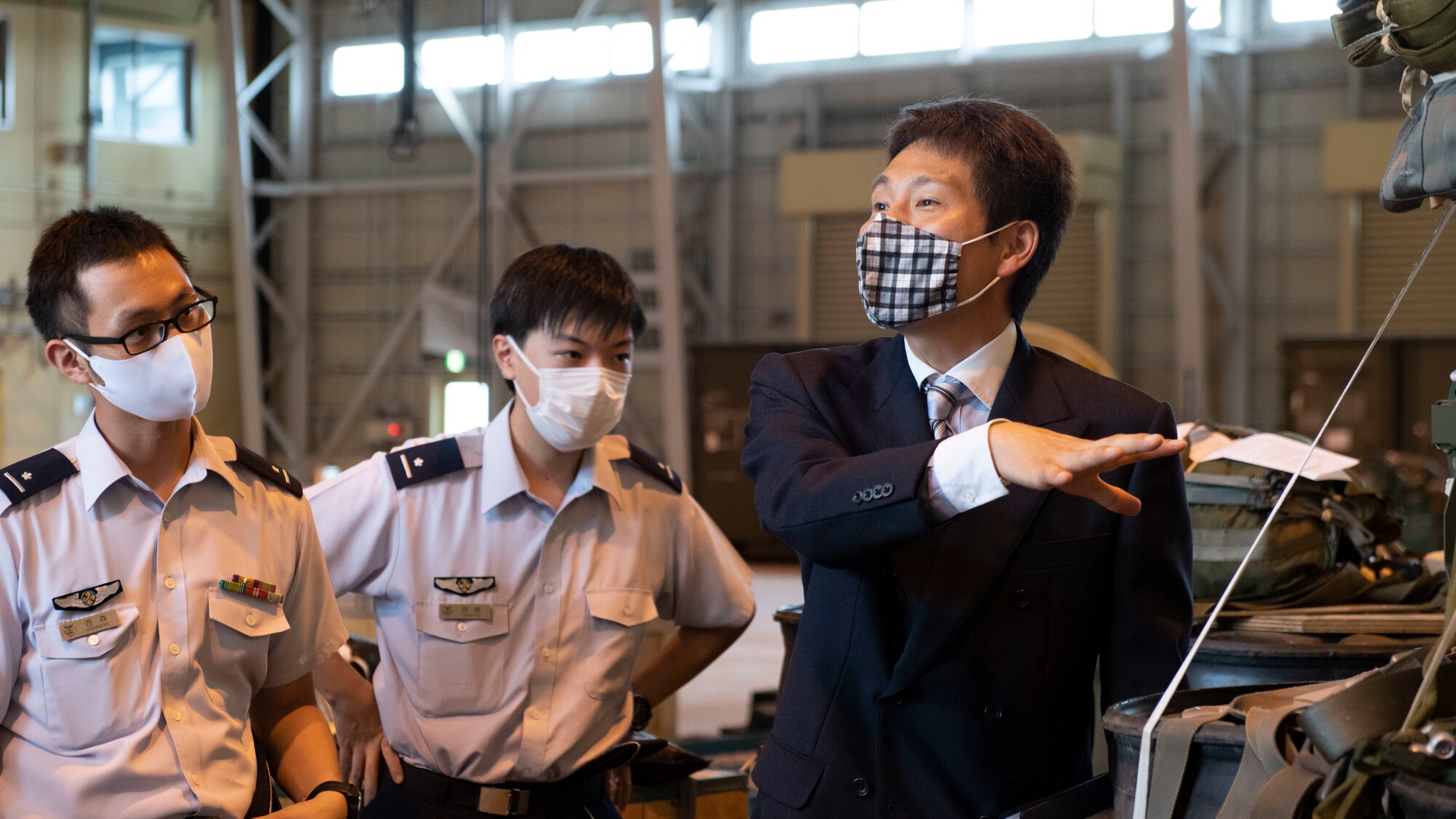 A Japanese translator in a suit gestures to cargo pallets