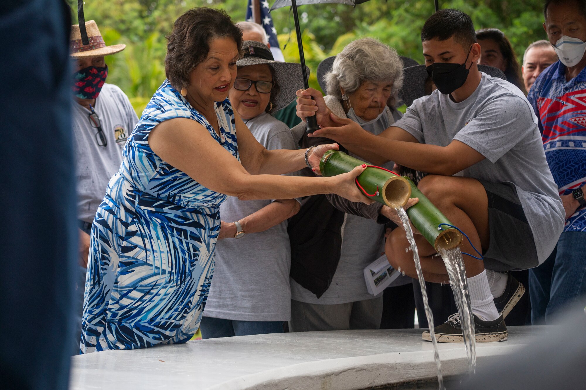 Two women pouring a cup of water into a fountain.