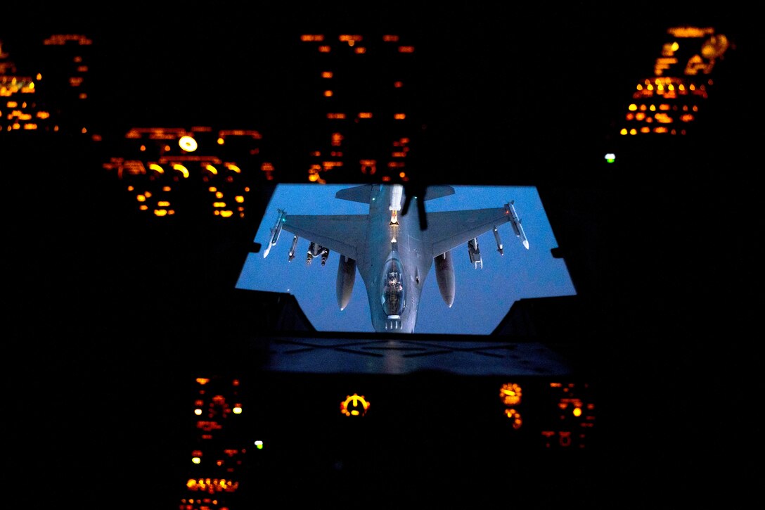 A military aircraft is seen from the inside of another aircraft flying above.