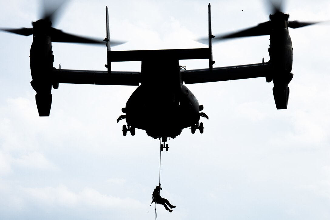 A Marine holds onto a rope as he rappels from a large aircraft.