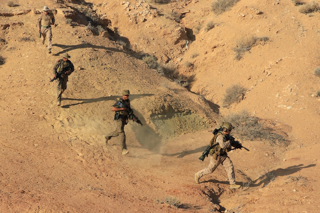 A Marine and Tunisian armed forces holding weapons run through a desert.
