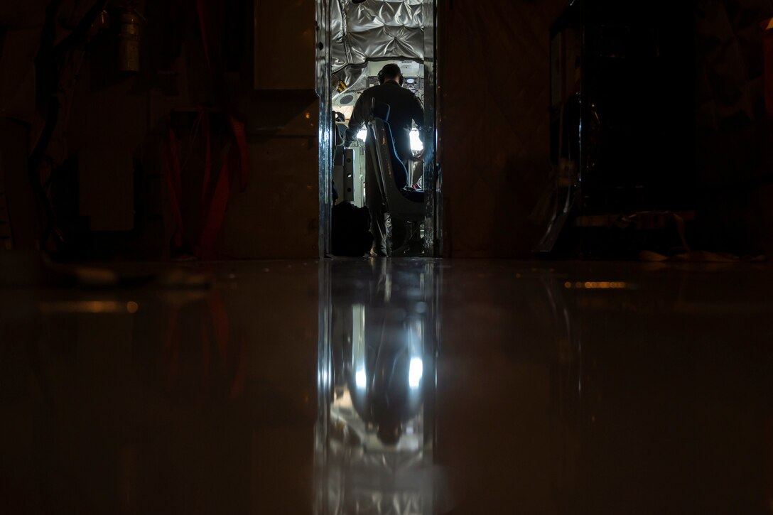 An airman stands in a cockpit in the dark.