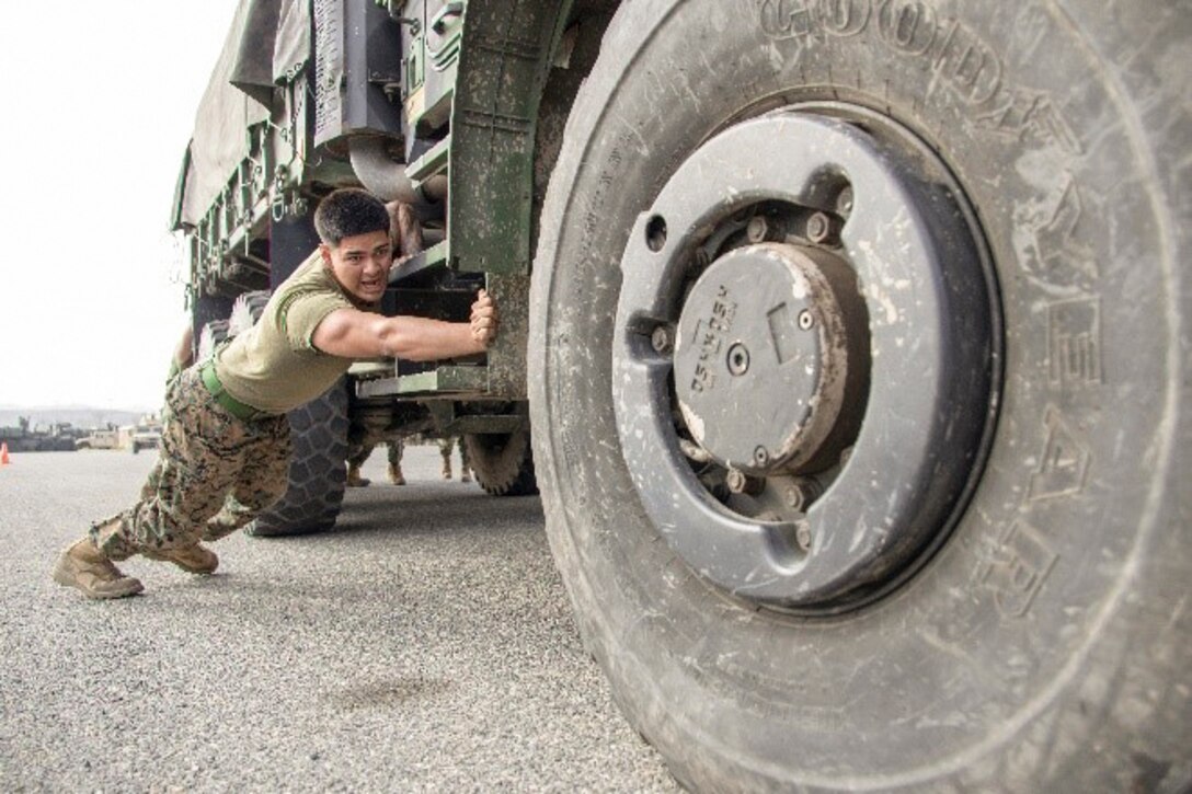 A Marine pushes a larges vehicle.