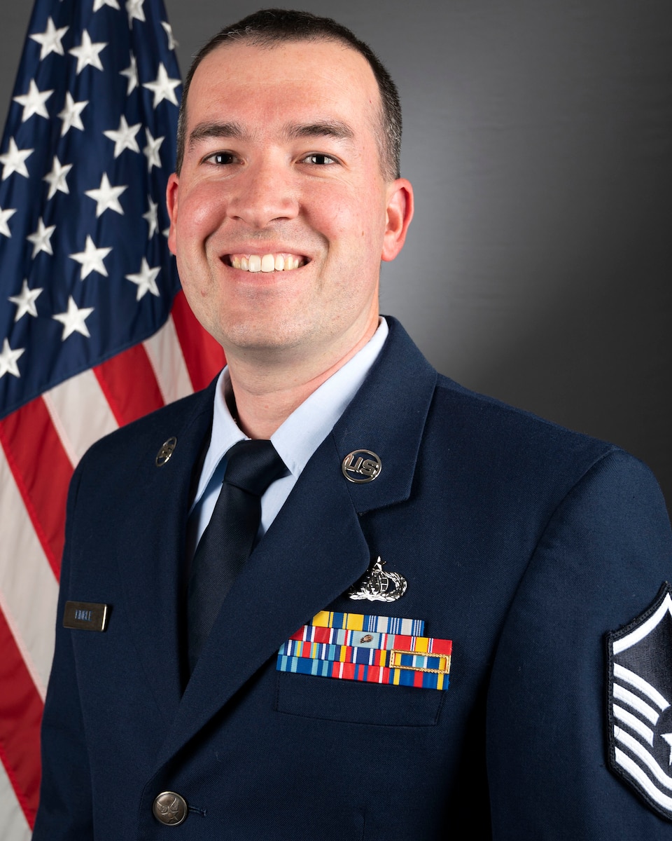 A headshot of MSgt Jordan Kimble in font of the American flag. He is wearing his blue service dress uniform.He is a member of Full Spectrum.