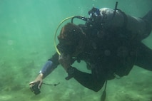 Diver swims through water while holding camera.