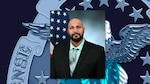 Official photo of a man in a black suit jacket and teal shirt in front of an American flag and blue background.