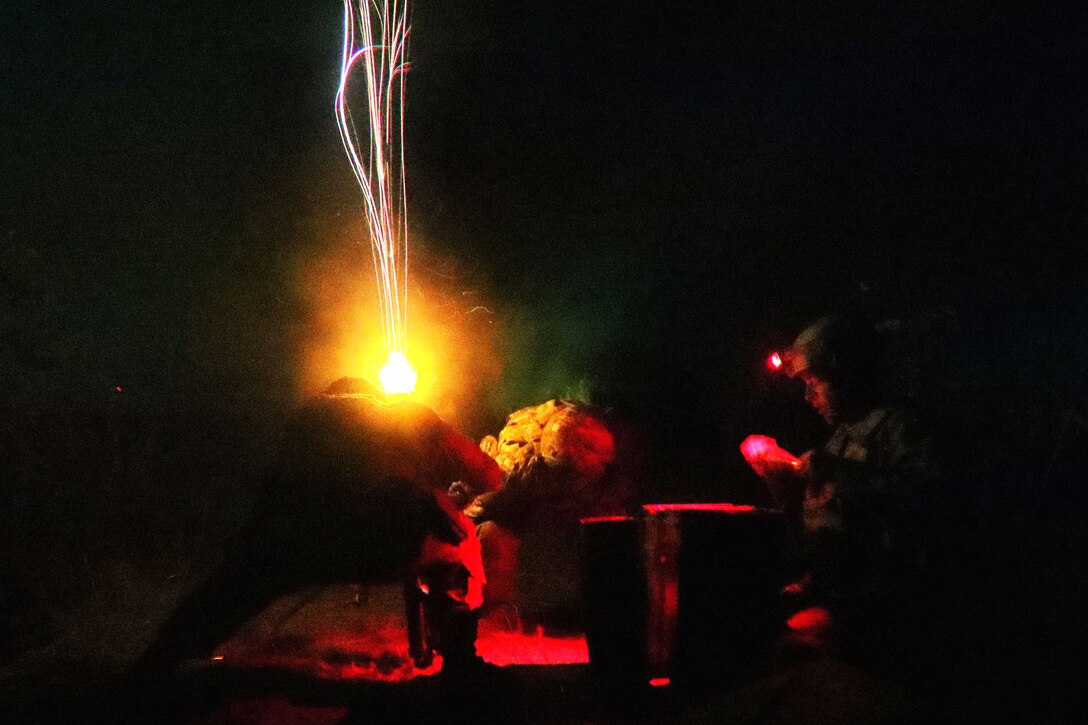 Soldiers operate a mortar system at night creating a small explosion.
