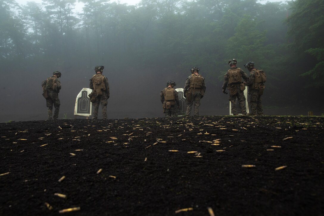 Marines examine targets at a range with shells in the foreground.