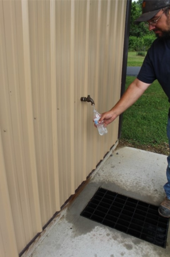 Man holds a water bottle underneath a water spigot.