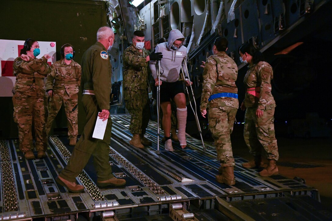 A group of 316th Operational Medical Readiness Squadron aerospace medical technicians and corpsmen from Walter Reed National Military Medical Center assist a wounded service member departing a C-17 Globemaster 3 to board a medical transport bus at Joint Base Andrews, Md., July 7, 2022