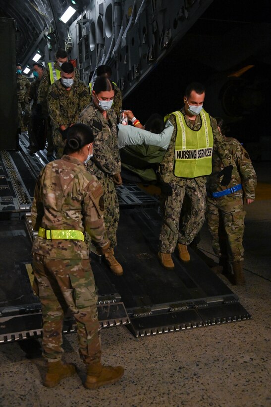 A group of 316th Operational Medical Readiness Squadron aerospace medical technicians and corpsmen from Walter Reed National Military Medical Center carry a wounded service member on a gurney from a C-17 Globemaster 3 to a medical transport bus at Joint Base Andrews, Md., July 7, 2022.