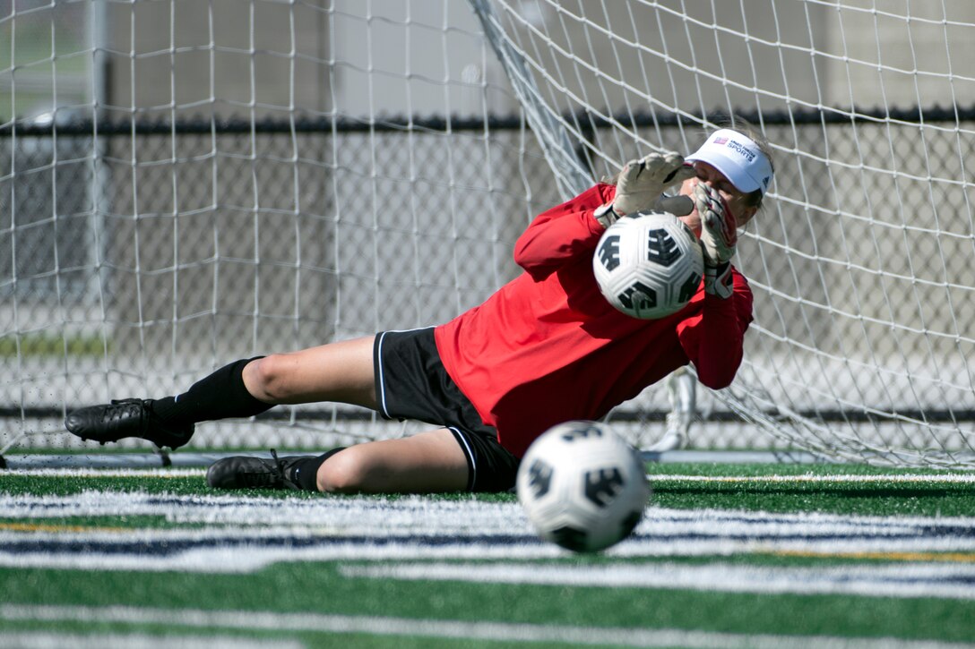 A goalie deflects a soccer ball.