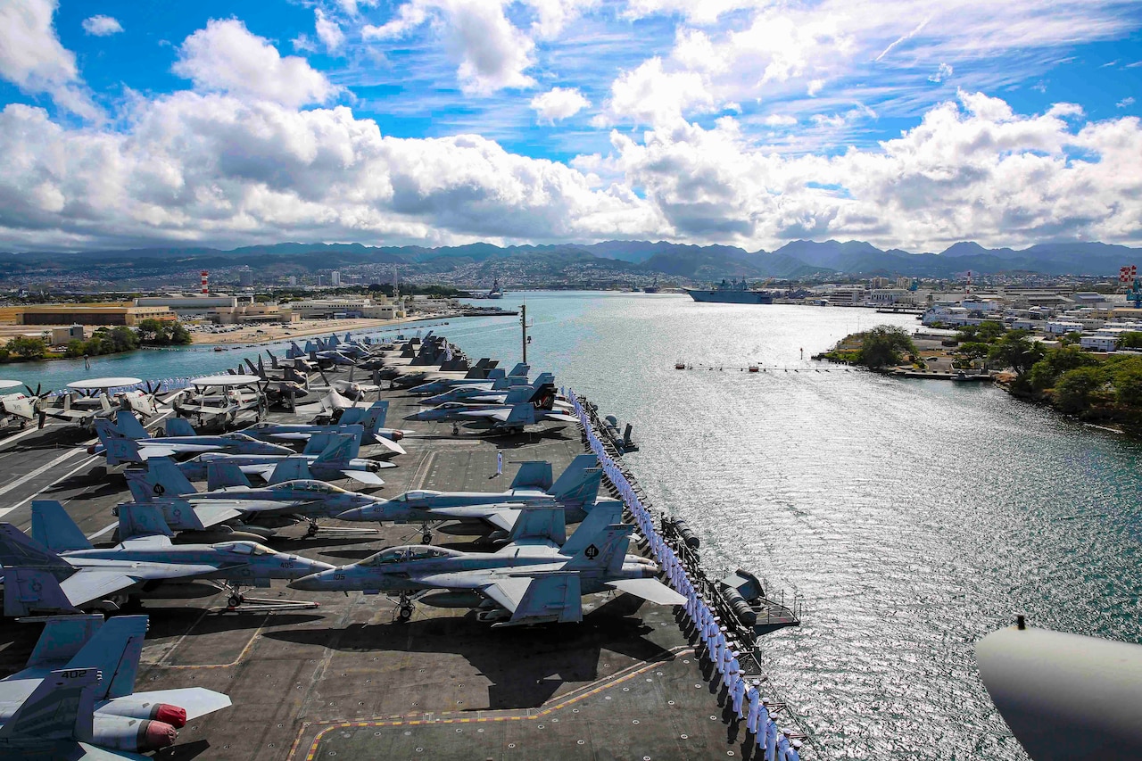 Aircraft parked on the deck of a ship that is traveling through waters.