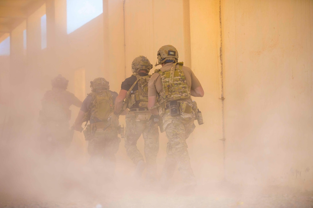Four soldiers move through a dust filled building.