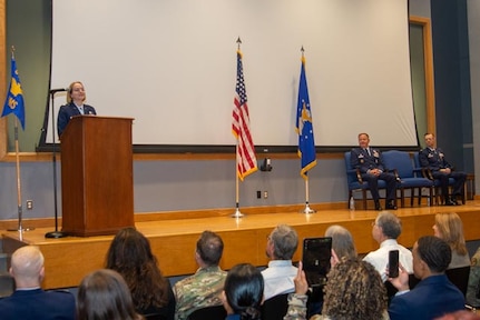 Three Air Force members are on a stage with two flags.
