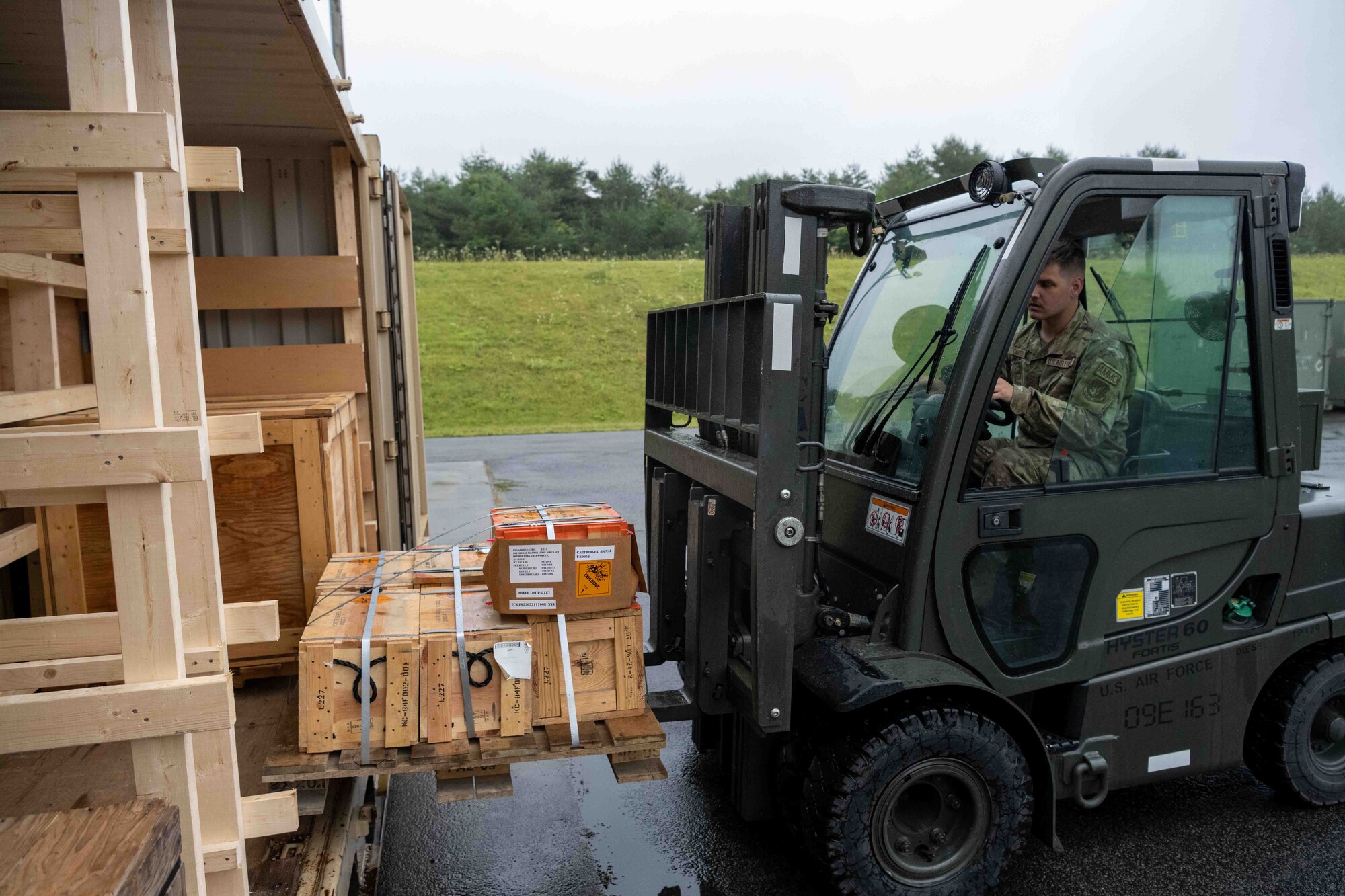 A military member places a pallet onto a shipping container with a fork lift.