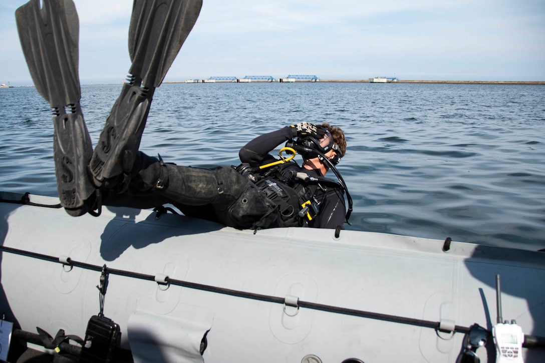 A diver does a backward dive into the water from a boat.