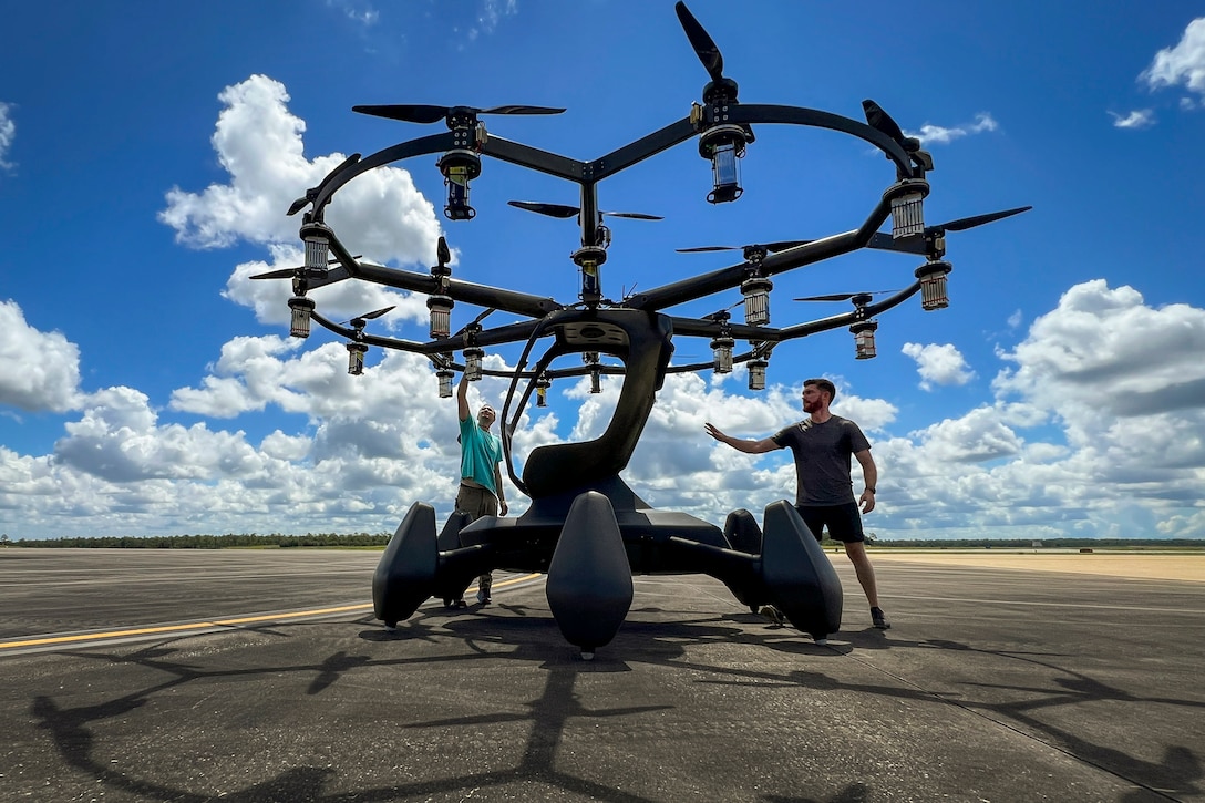 Two people work on a large electric aircraft on a paved lot.