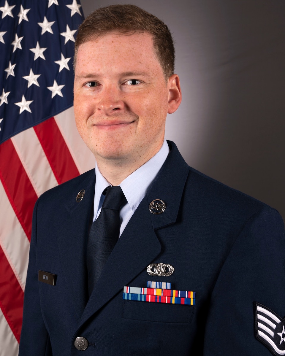 Official Headshot of SSgt Brian Bean in front of the American flag. He is wearing his blue service dress uniform.