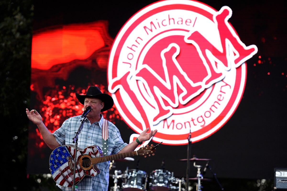 A man holding a guitar painted like the U.S. flag speaks into a microphone on a stage.