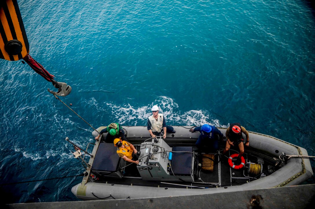 Sailors in an inflatable boat move alongside a ship.