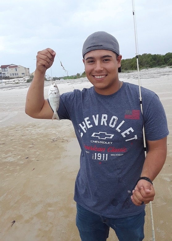 A sailor in civilian clothes holds up a fish on a line.