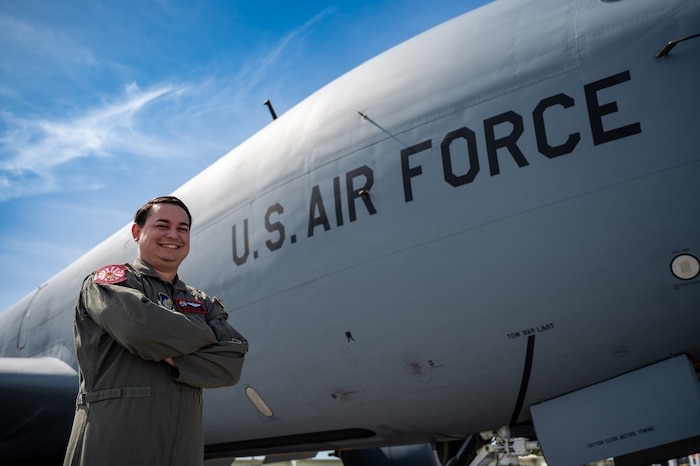 Smiling Airman in flight suit with arms crossed standing beside U.S. Air Force plane