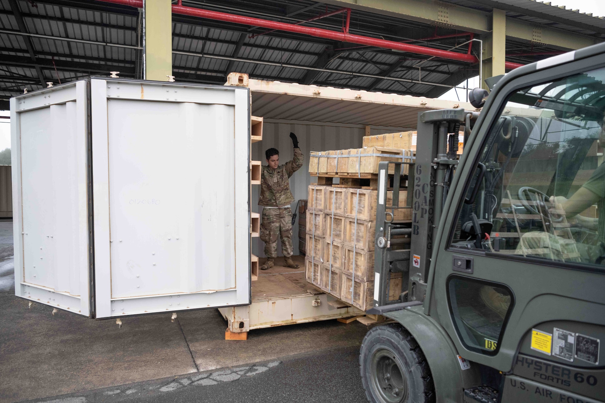 A military member puts a pallet onto a shipping container.