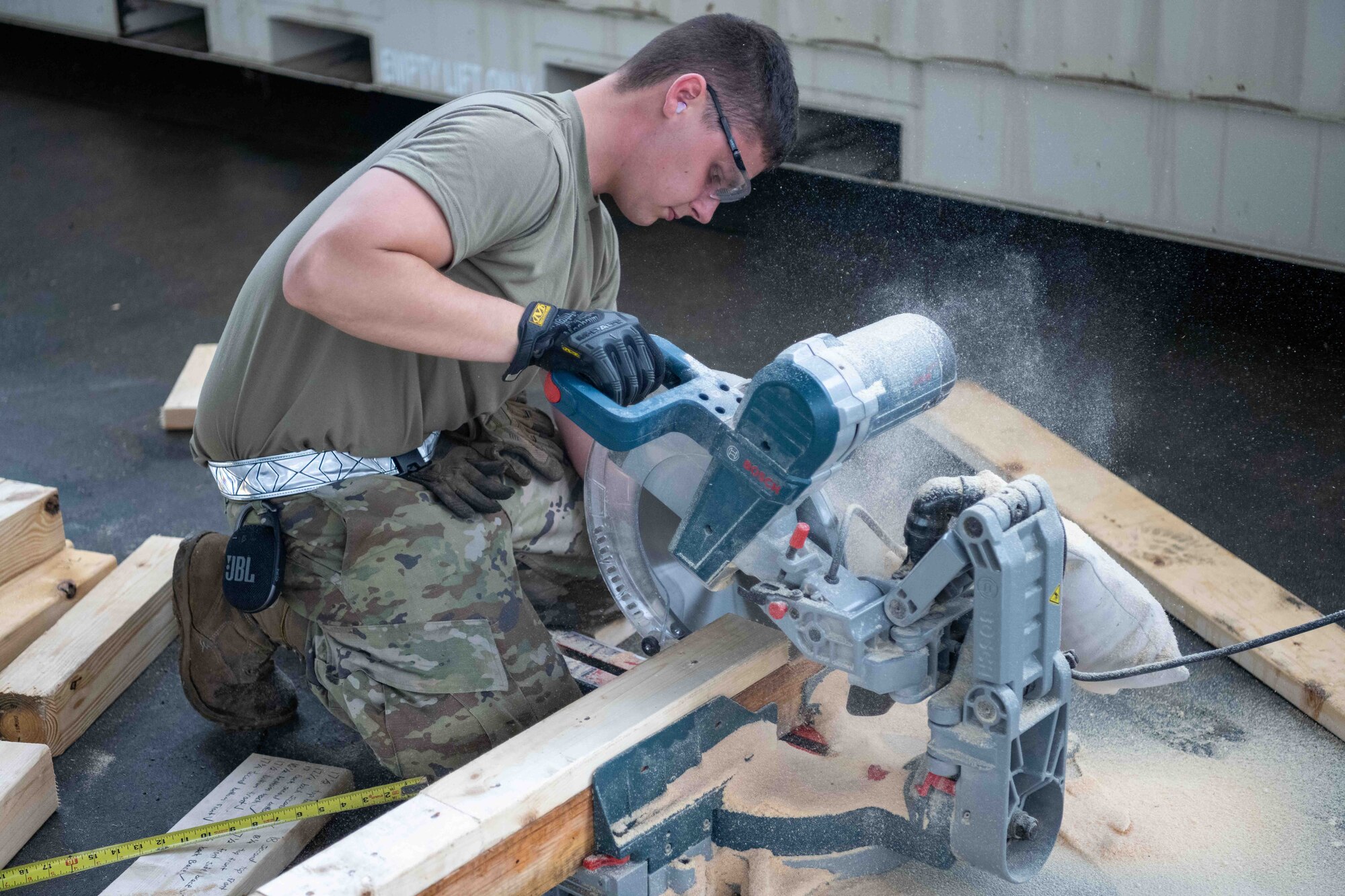 A military member saws a plank of wood to make a brace.