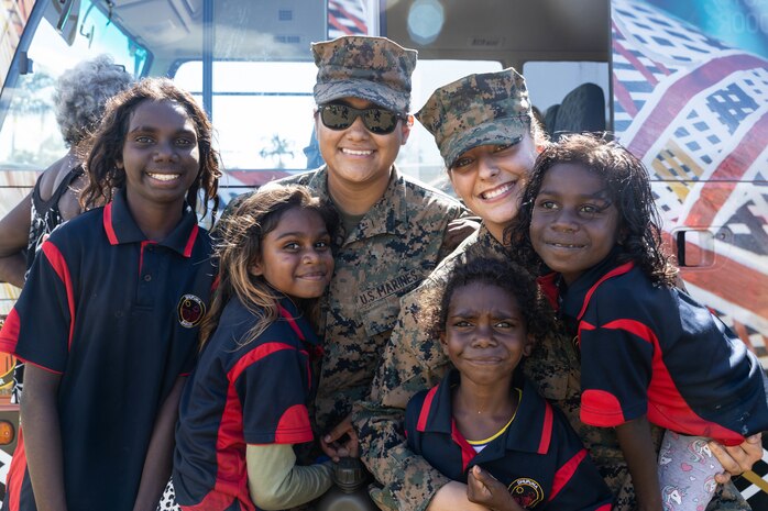 U.S. Marine Corps Lance Cpl. Isabel Plata (left), an embark specialist, and Cpl. Qearia Braden, a transmissions system operator, with Combat Logistics Battalion 5, Logistics Combat Element, Marine Rotational Force-Darwin 22, pose for a photo with children from a local school in Nhulunbuy, NT, Australia, May 19, 2022. Exercise Crocodile Response participants hosted a community event to allow citizens of Nhulunbuy to view equipment and interact with MRF-D 22, members of the Australian Defence Force and the Indonesian National Armed Forces.