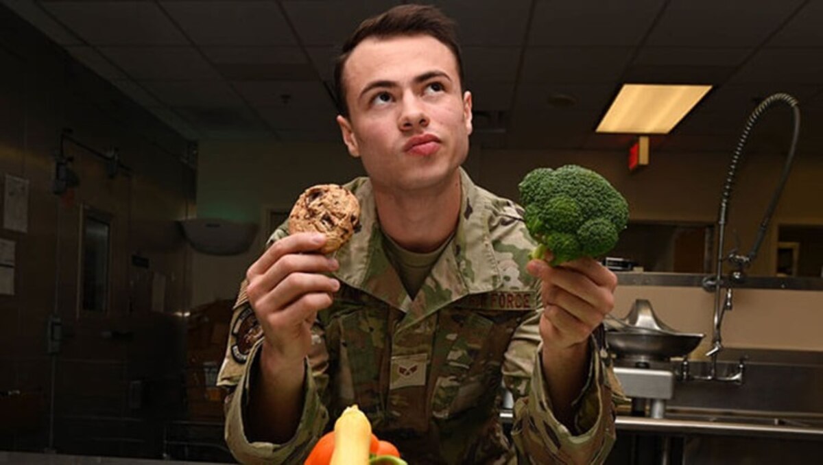 Image of an Airman holding a cookie and broccoli.